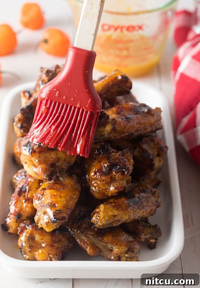 Using a red pastry brush peach habanero glaze on a plateful of chicken wings.