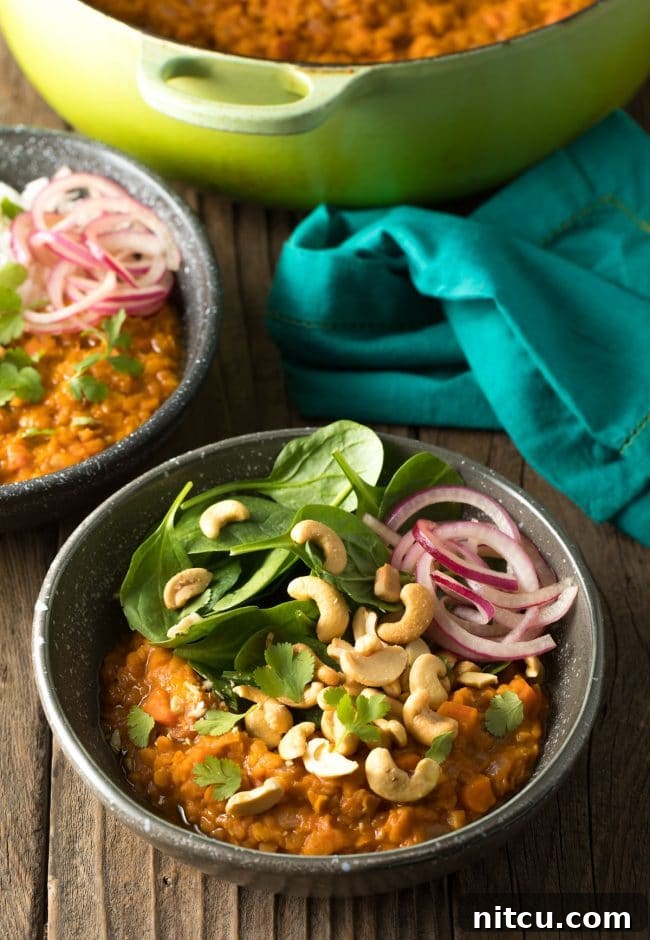 Bowl of curry with fresh baby spinach, all topped with whole raw cashews, red onion slices, and chopped fresh cilantro.