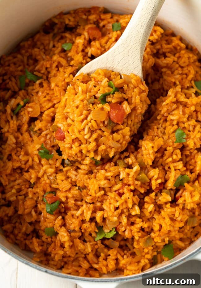 A close-up view of a pot of cooked Mexican rice, with a wooden spoon partially submerged, showcasing the texture and vibrant color of the fluffy grains. The steam still rises gently from the rice, indicating it's fresh and warm, ready to be served as a delicious side dish.