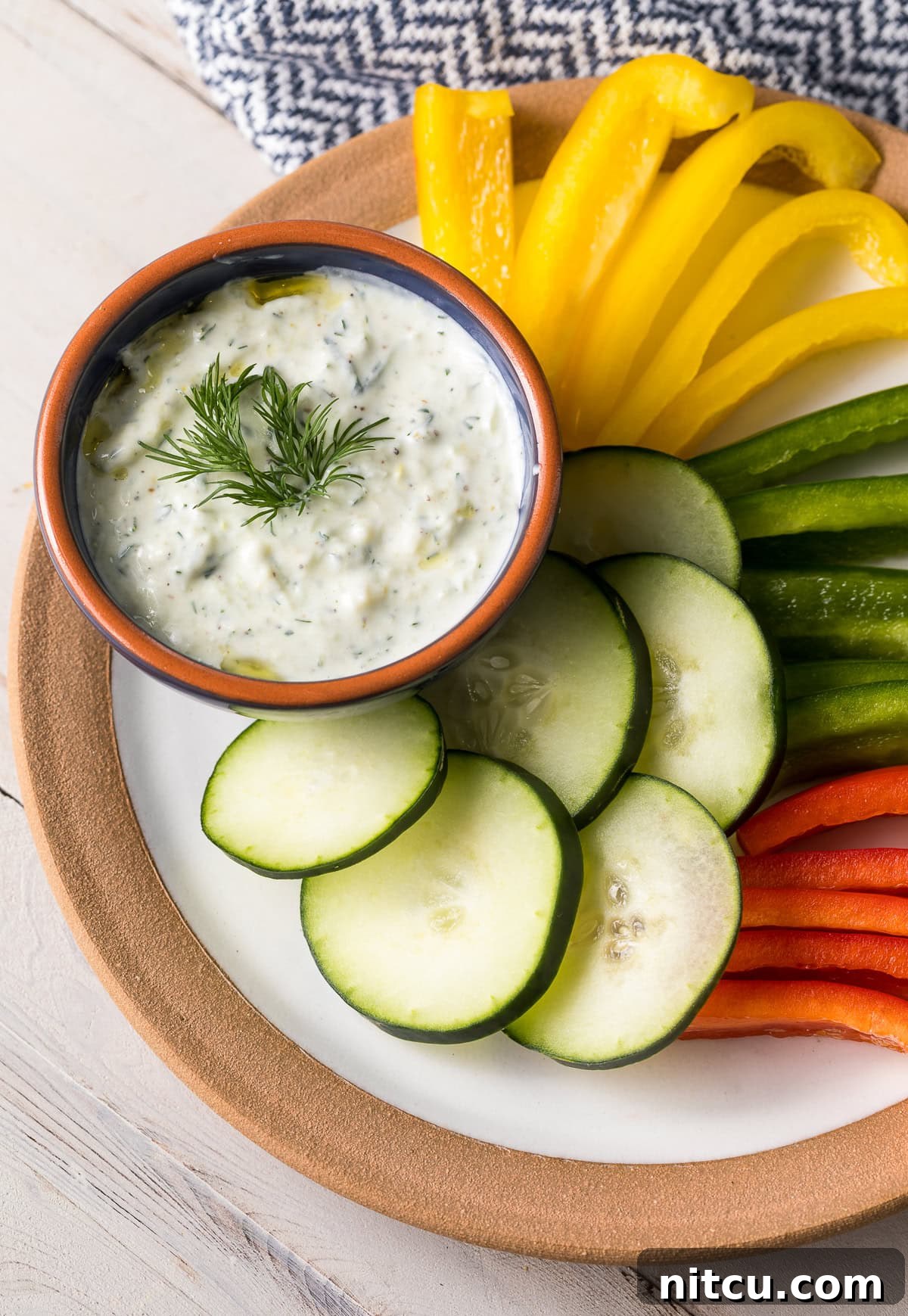 Tzatziki dip in an orange and blue bowl placed on a serving platter next to cut up veggies.
