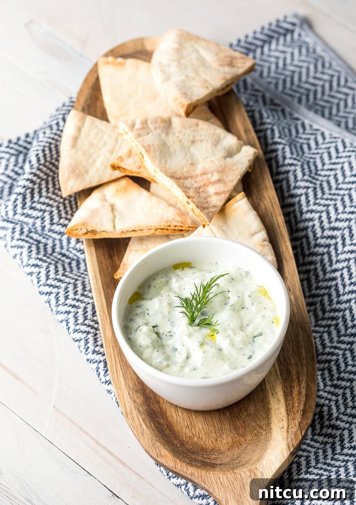 Tzatziki dip in a white bowl, placed on a wood platter with pita bread.