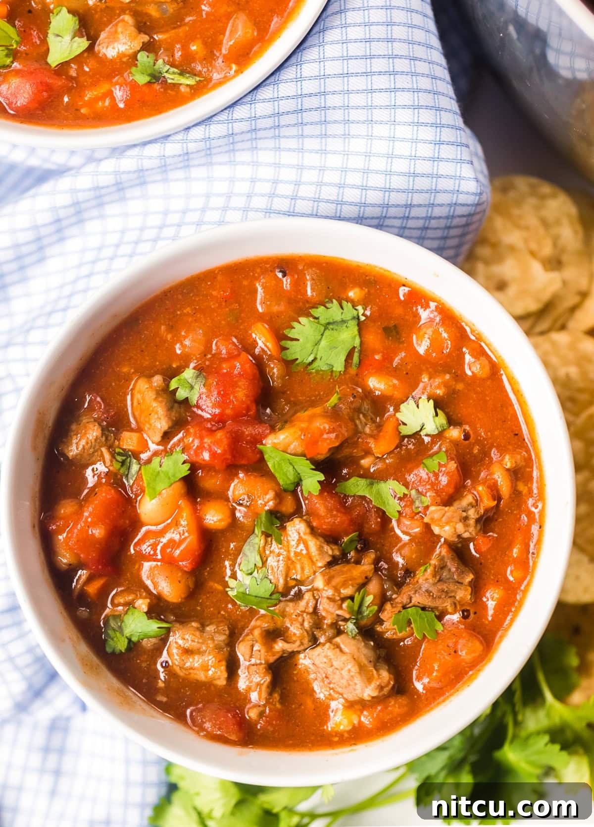Overhead shot of a white bowl filled with richly colored Chili Recipe with Beer, topped with vibrant green cilantro.