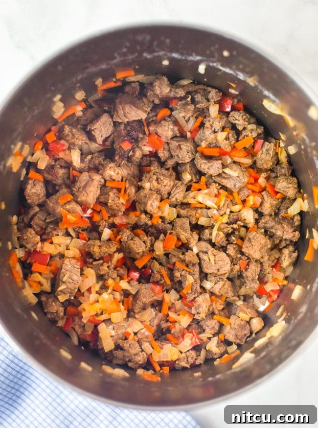 Diced steak and vibrant vegetables sizzling in a large stock pot, preparing the flavorful base for the chili.