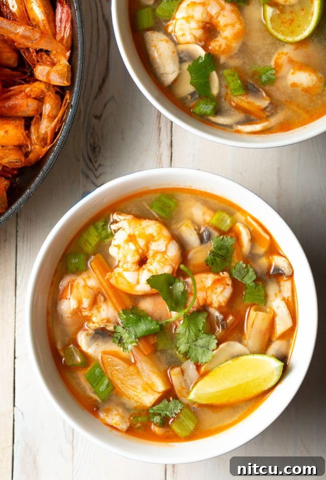 Overhead shot of a vibrant bowl of Tom Yum soup, garnished with fresh cilantro and bright lime wedges, showcasing its rich colors and enticing aroma.
