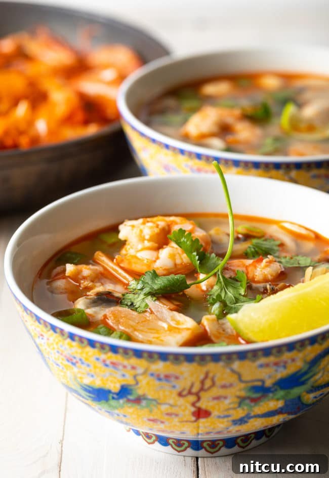 Two steaming bowls of Thai Hot and Sour Soup, artfully garnished with fresh cilantro and a lime wedge, ready to be enjoyed.