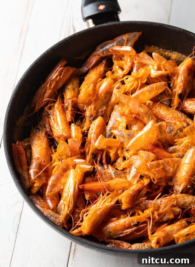 Shrimp heads are sautéing in a skillet with oil, turning red and crispy to create flavorful shrimp oil for the Tom Yum soup.