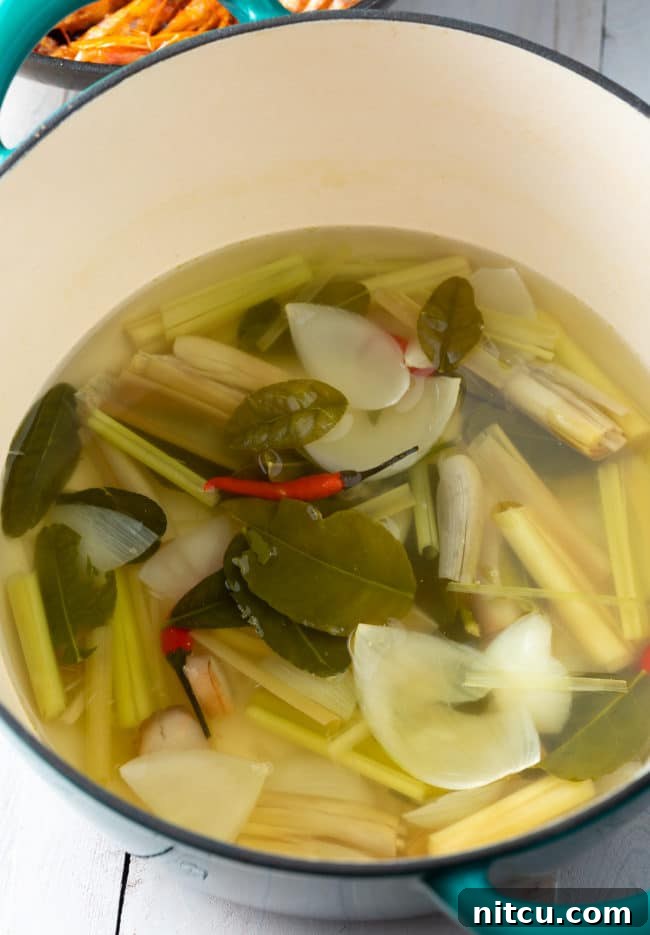 Aromatic kaffir lime leaves and stalks of lemongrass infusing in a simmering broth, releasing their fragrant essences.