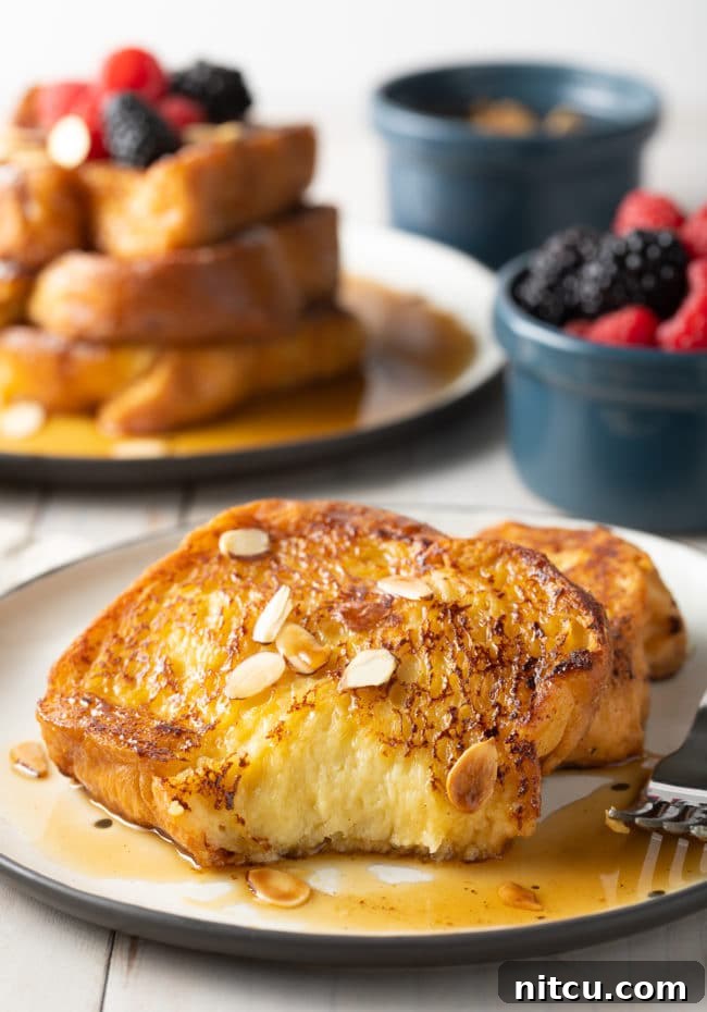 Two slices of pain perdu with a bit taken out of it on a white plate.
