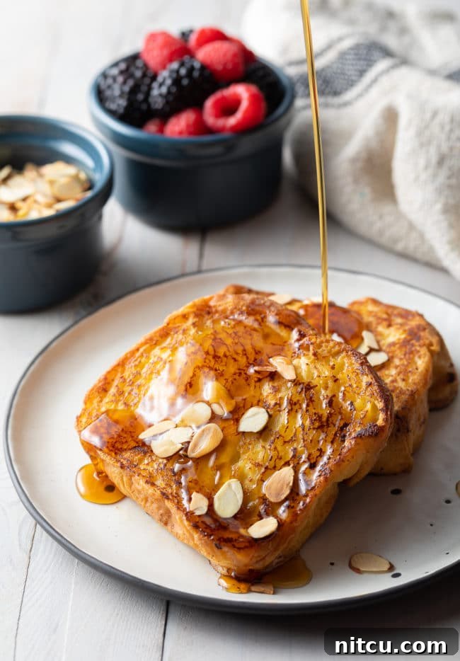 Two slices of pain perdu with maple syrup drizzling on top.