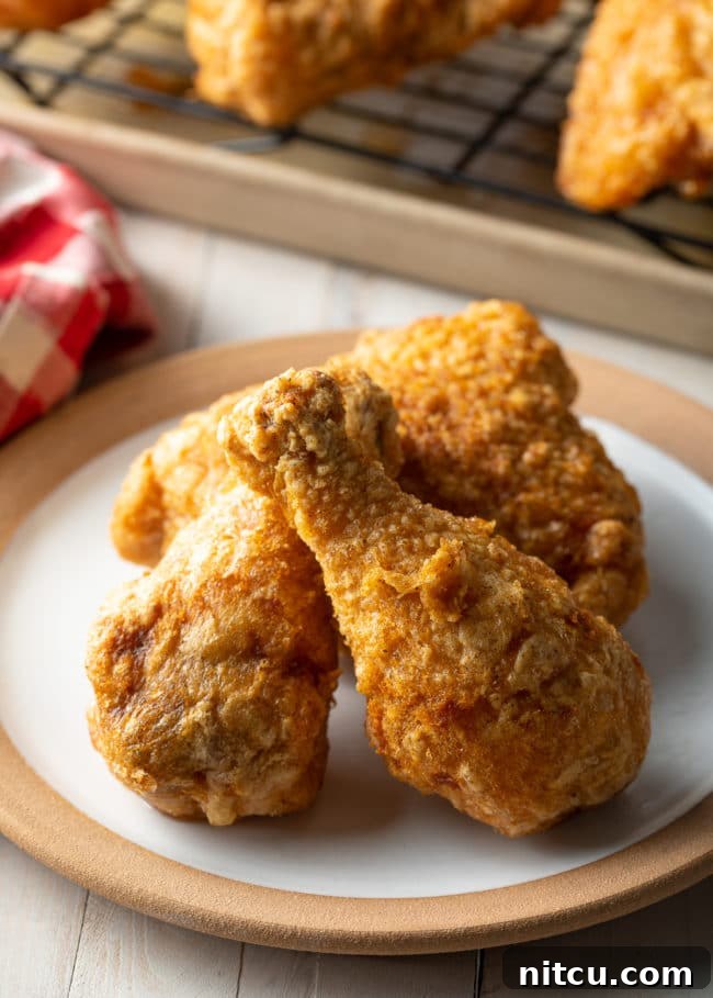 Three pieces of golden-brown tavern fried chicken on a white plate, showcasing its light, crispy skin.