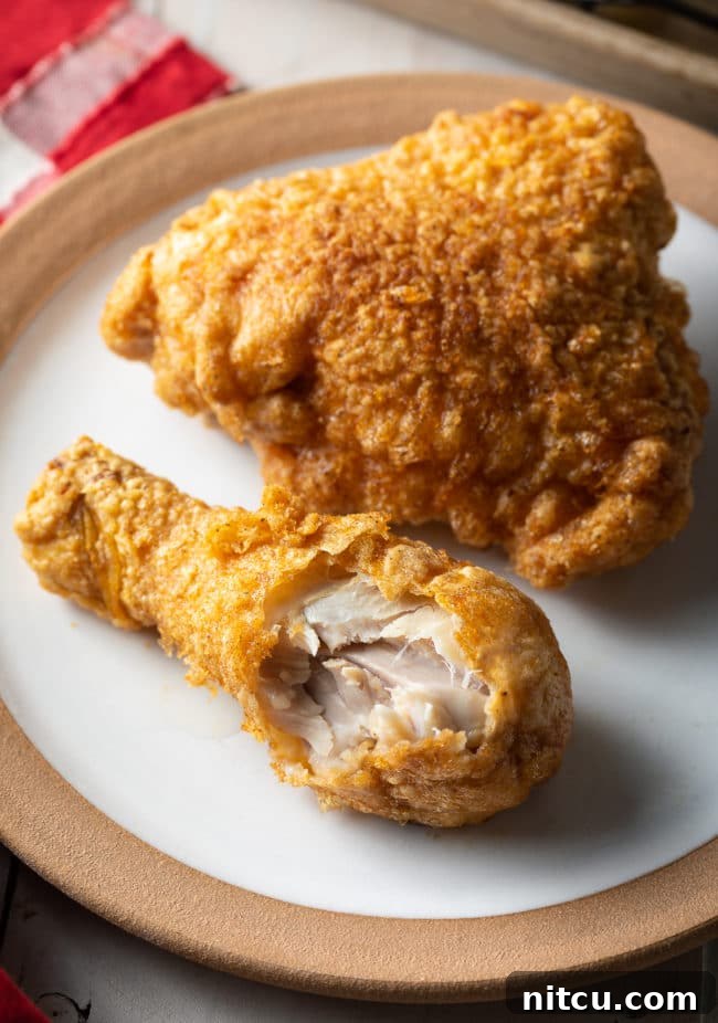 Top-down view of a breaded fried chicken thigh and drumstick on a plate, with a bite taken from the drumstick.