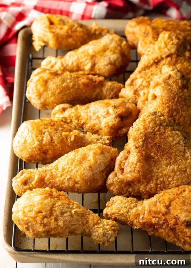 Several pieces of golden-brown fried chicken legs and thighs resting on a wire rack over a baking sheet, allowing excess oil to drip.
