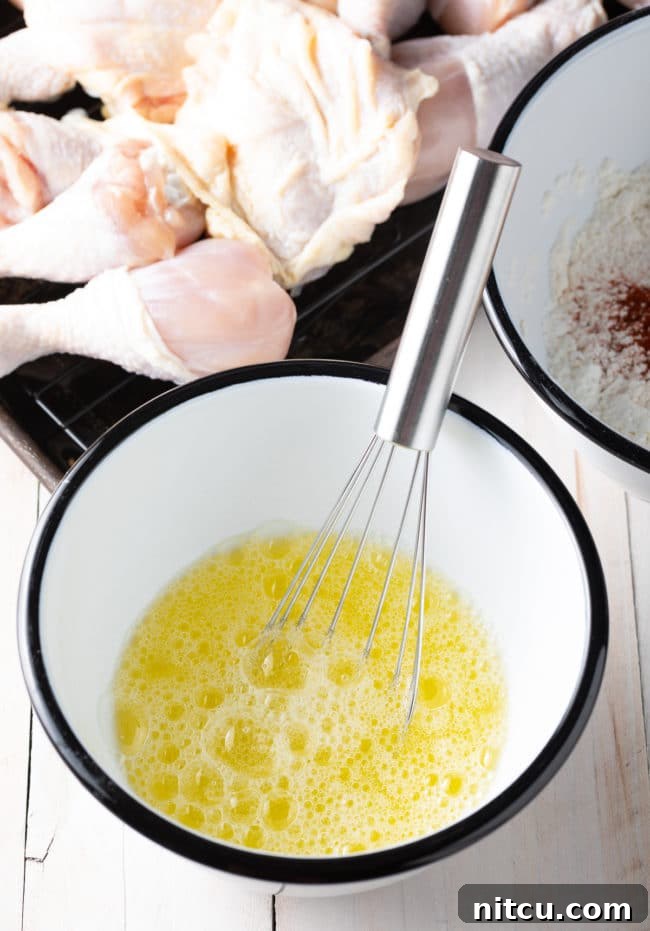 Whisked egg whites in a white mixing bowl with a metal whisk, showing their frothy texture.