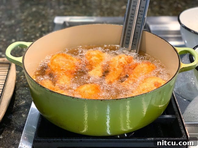 Golden-brown chicken pieces frying in hot oil in a large green Dutch oven, with tongs visible for turning.