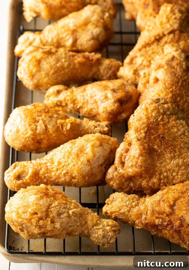 Several pieces of perfectly fried chicken legs and thighs arranged on a wire rack over a baking sheet, glistening golden-brown.