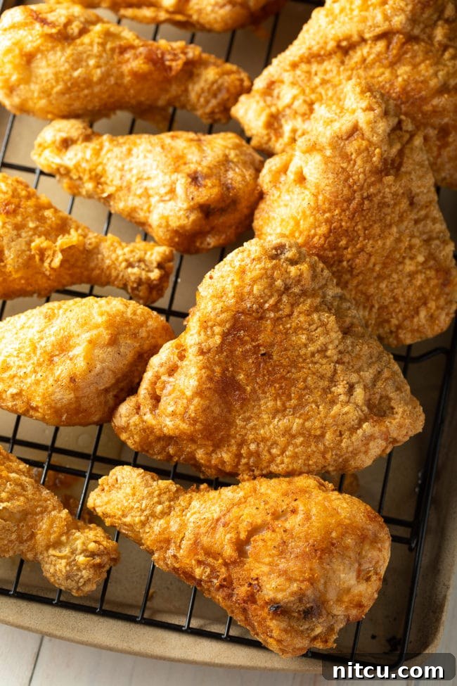 Several pieces of golden-brown fried chicken legs and thighs neatly arranged on a wire rack over a baking sheet.