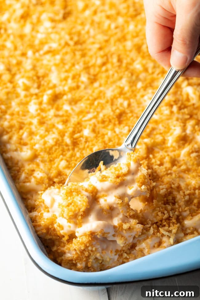 Side view of baked macaroni with cream cheese in a casserole dish with a spoon taking out a portion