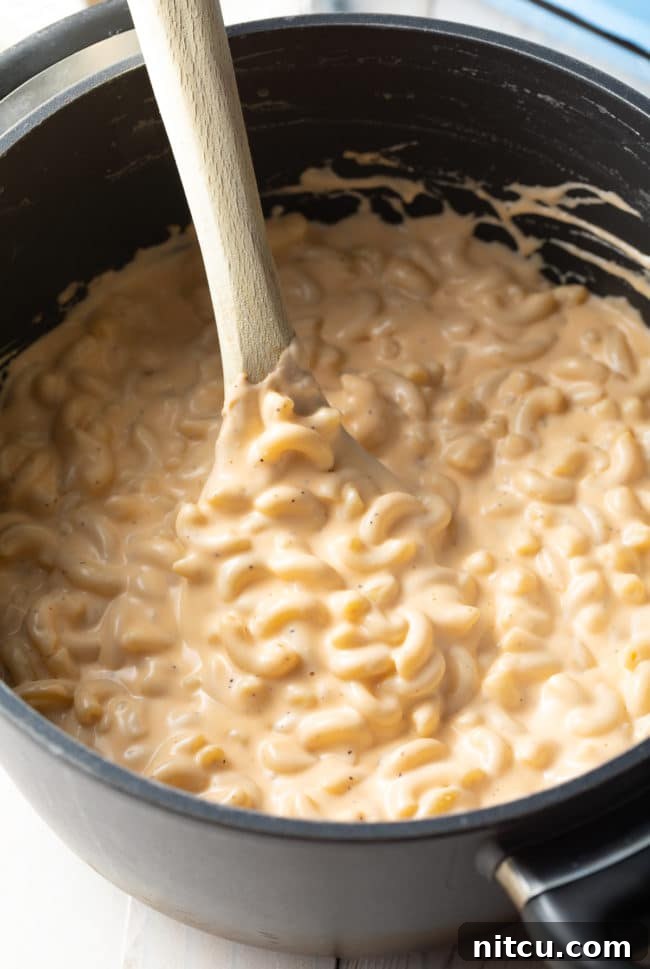 Best Homemade Mac and Cheese - Top view of a wooden spoon stirring the stovetop pasta in cheese sauce