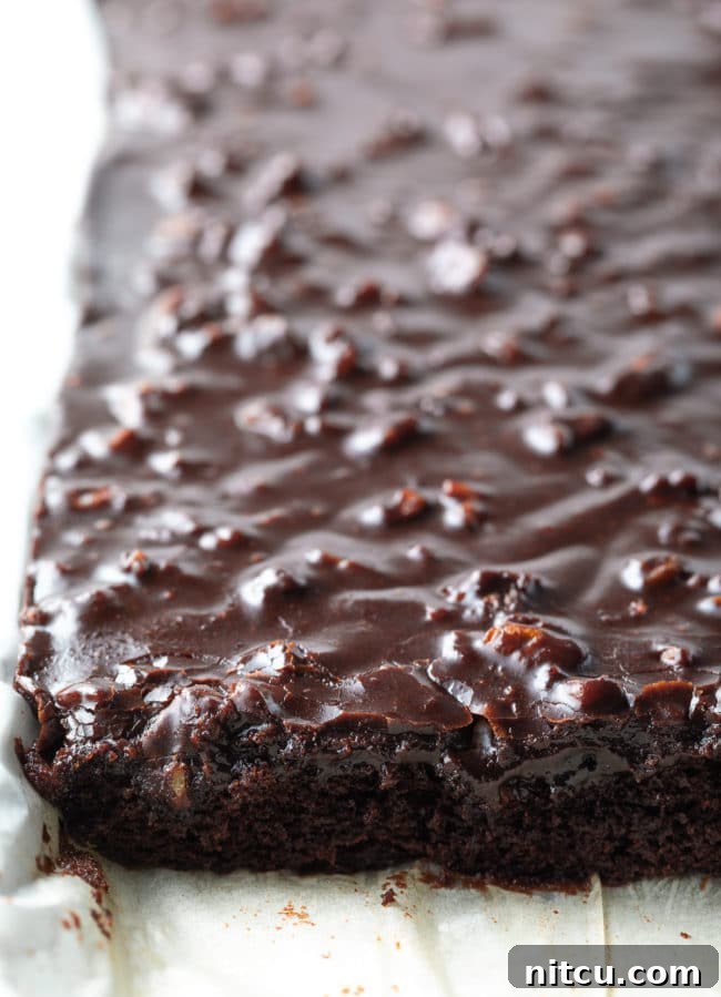 Texas Sheet Cake on a pan lined with parchment paper with part of the cake cut into.