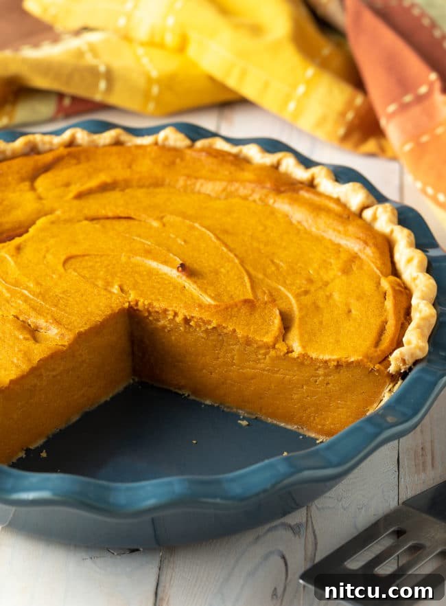 A whole, easy-to-make sweet potato pie with several slices already removed, revealing its creamy golden interior and inviting texture. It sits on a rustic wooden surface, highlighting its homemade appeal.