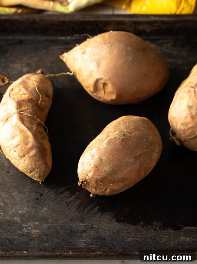 Baked sweet potatoes, whole and tender, arranged on a baking sheet, illustrating the initial step in preparing an old-fashioned sweet potato pie from scratch.