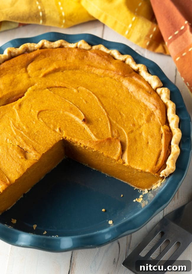 An easy-to-make sweet potato pie, freshly baked, with a few slices removed to show its appealing texture and readiness for serving during a festive meal.