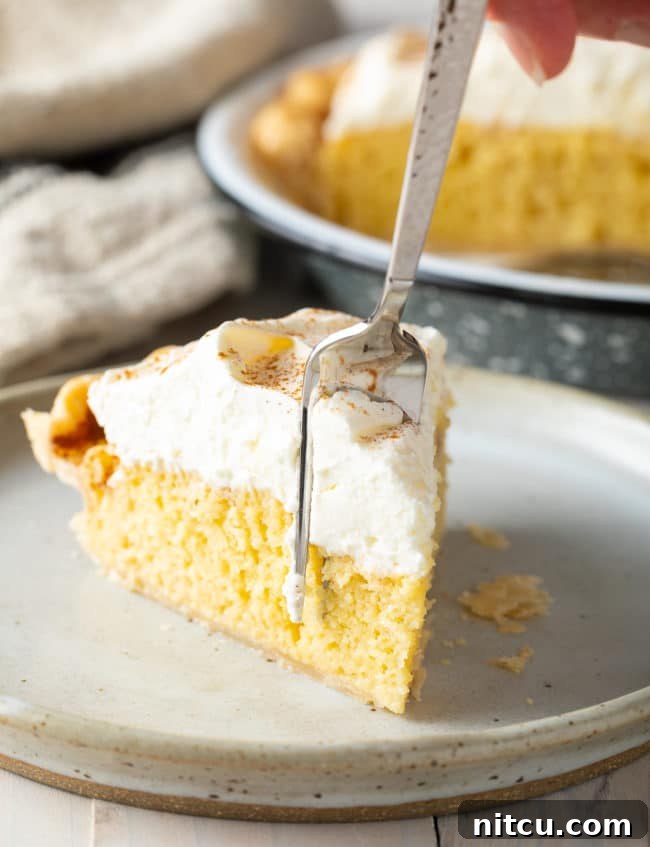 A perfectly sliced piece of creamy Tres Leches Pie on a white plate, served with a fork, showing off its rich layers.