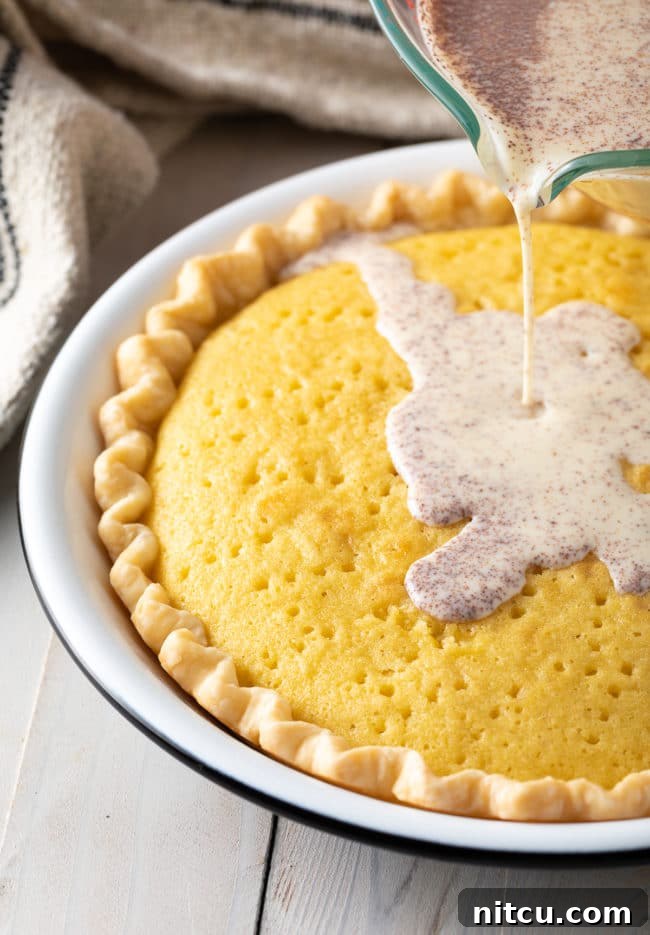 A freshly baked Tres Leches Pie, still in its pan, with the three milks being slowly poured over the poked sponge cake.
