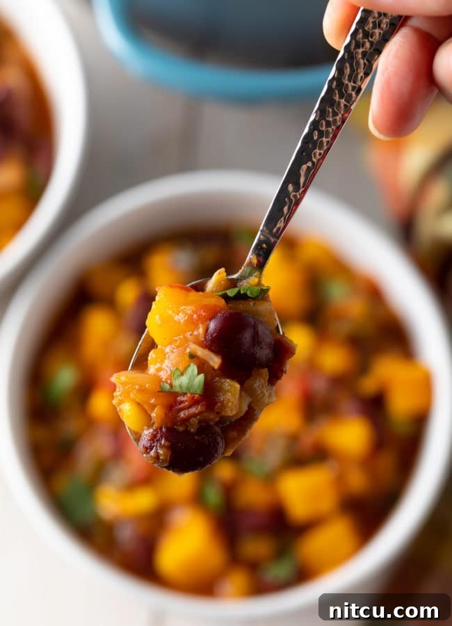 A close-up of a spoonful of crock pot butternut squash chili, highlighting its vibrant colors and rich texture.