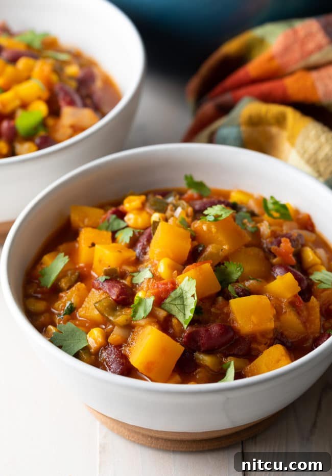 A steaming bowl of vegetarian chili, showcasing chunks of butternut squash, kidney beans, and corn, garnished with fresh cilantro.