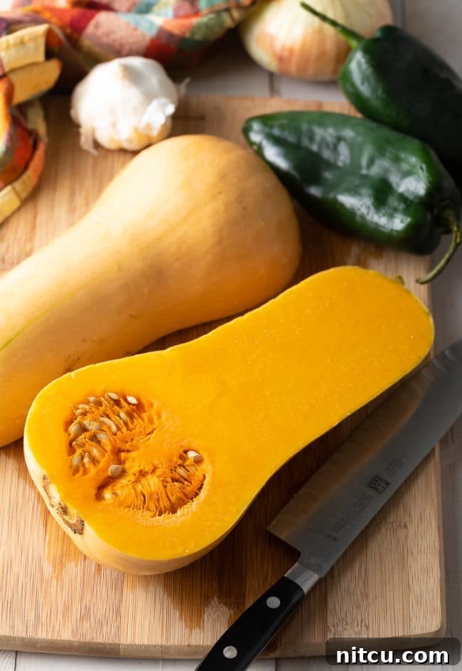 Fresh ingredients for Butternut Squash Chili laid out on a wooden table, including whole butternut squash, poblano peppers, onions, and cans of beans and tomatoes.