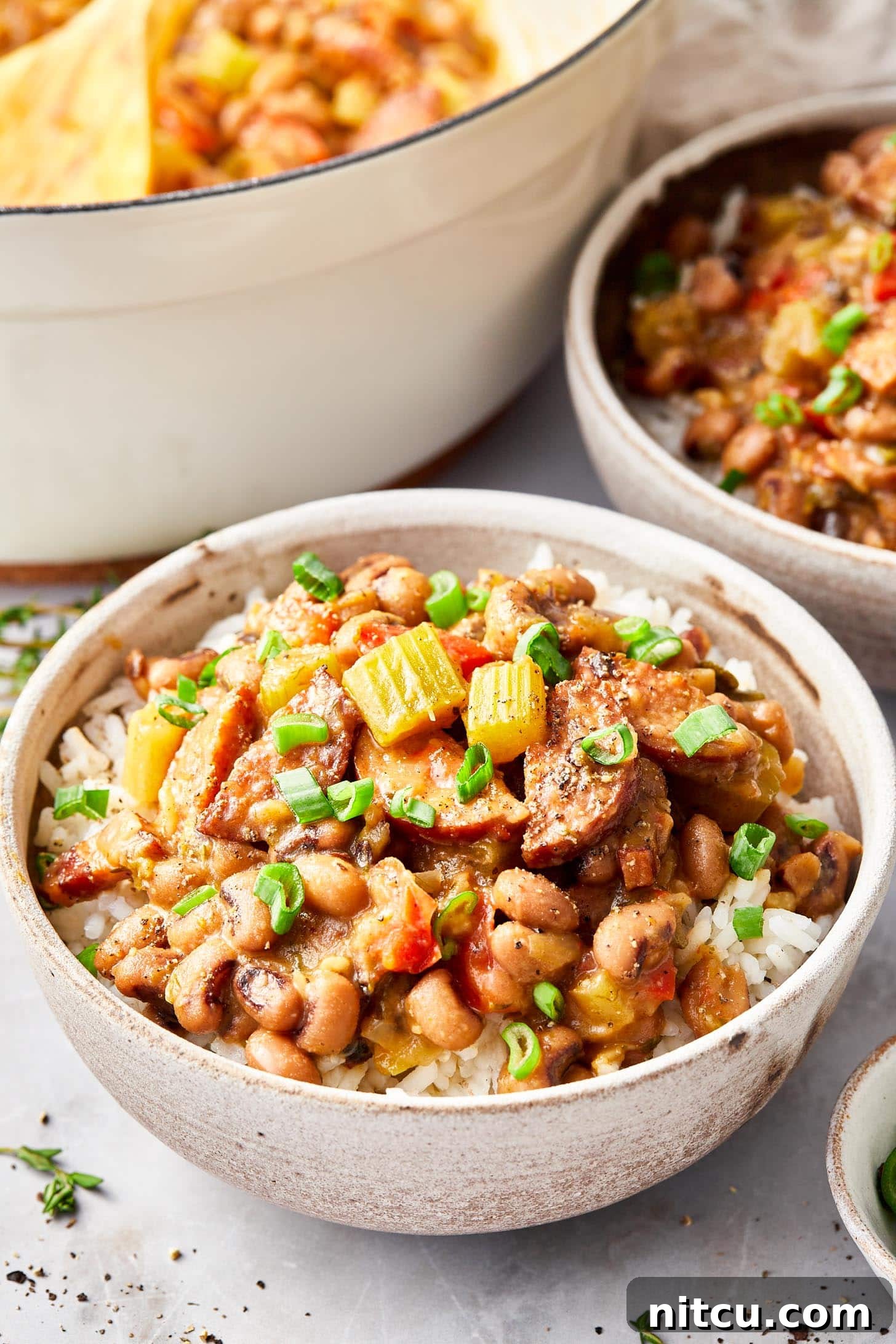 A vibrant closeup of Hoppin' John in a rustic bowl, showcasing tender black-eyed peas, smoky sausage, and fresh herbs.