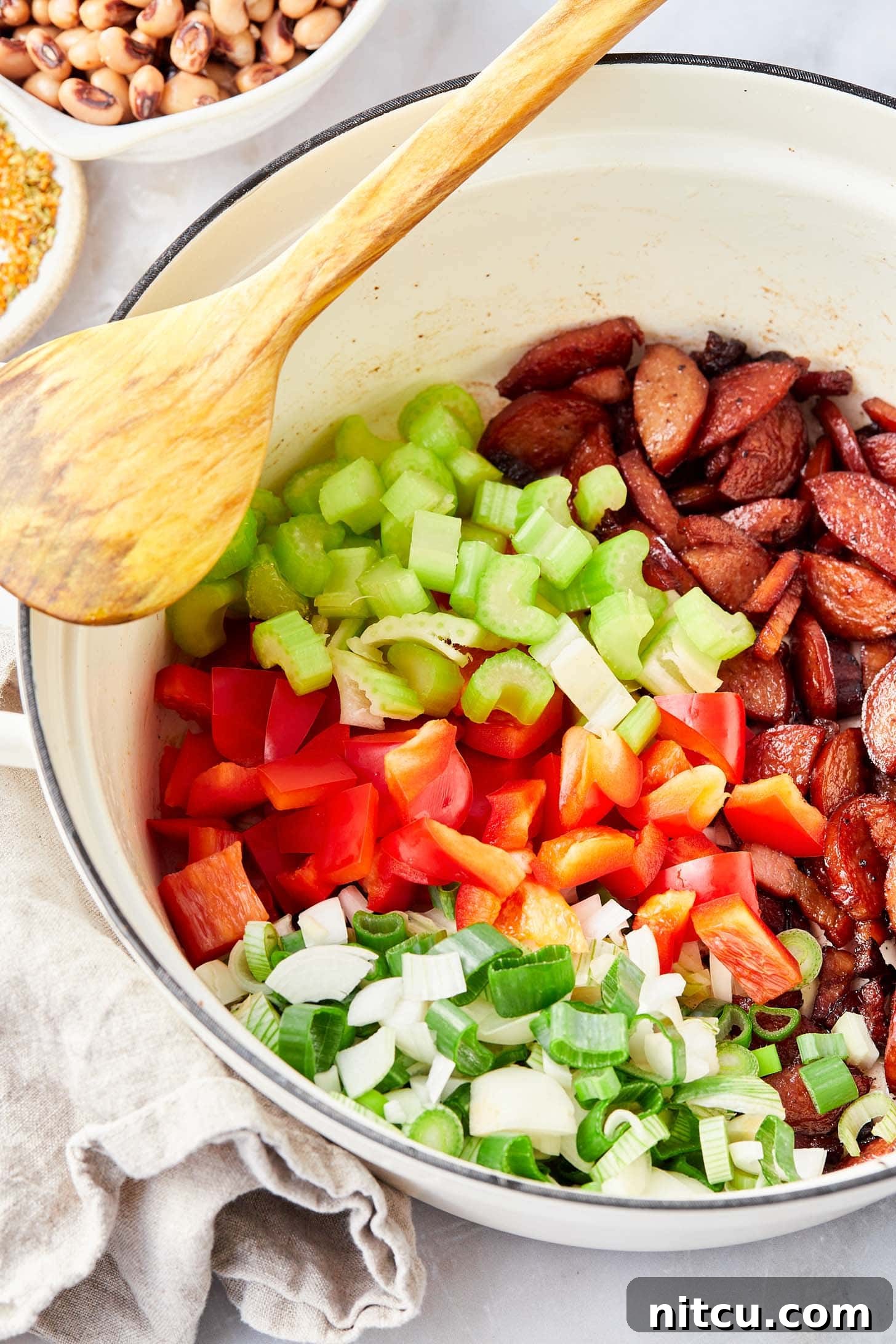 Colorful medley of onions, celery, bell peppers, and jalapeño sautéing in a skillet with browned sausage.