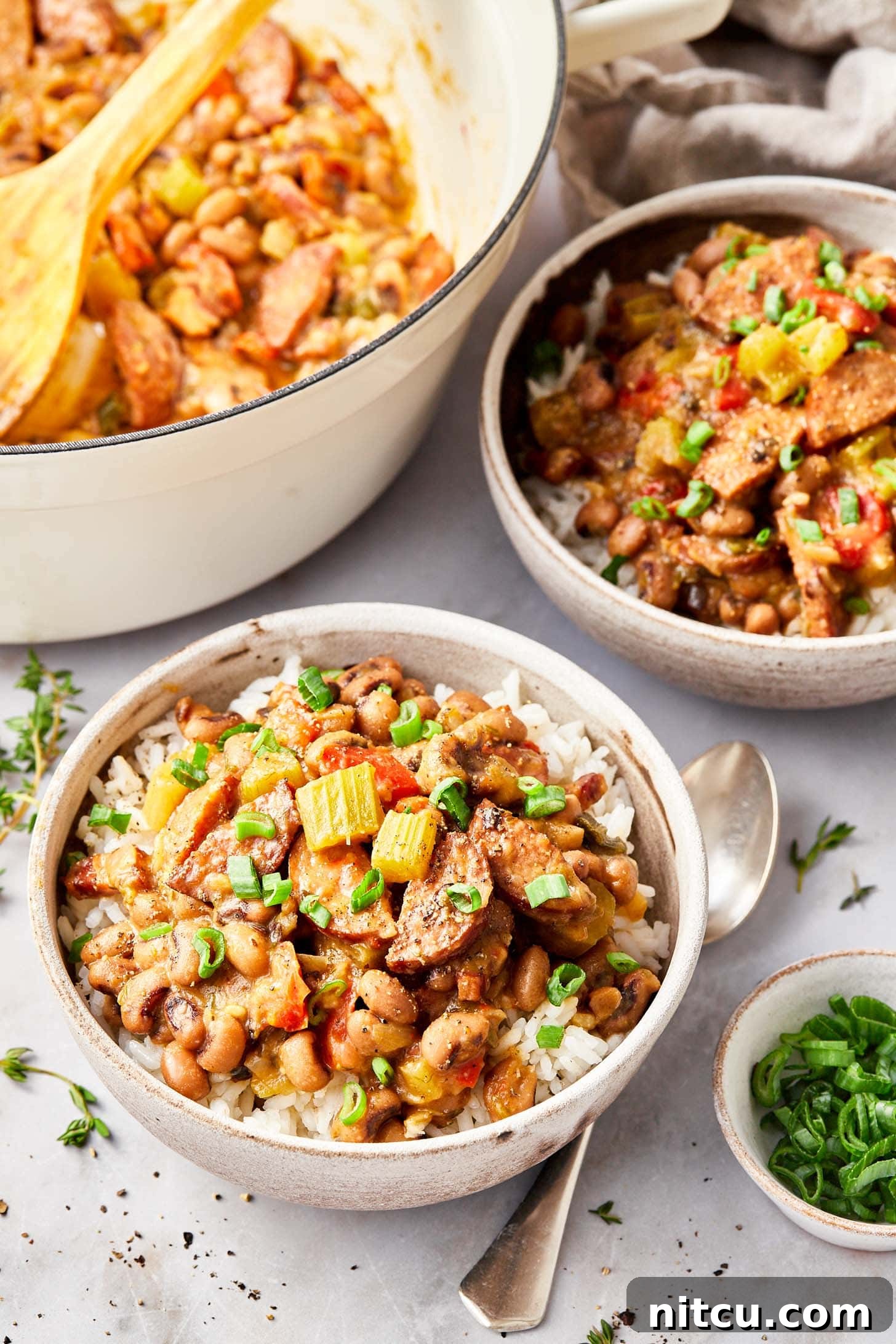 A beautifully plated bowl of Hoppin' John over rice, garnished with vibrant green onions, with a small dish of extra green onions on the side.