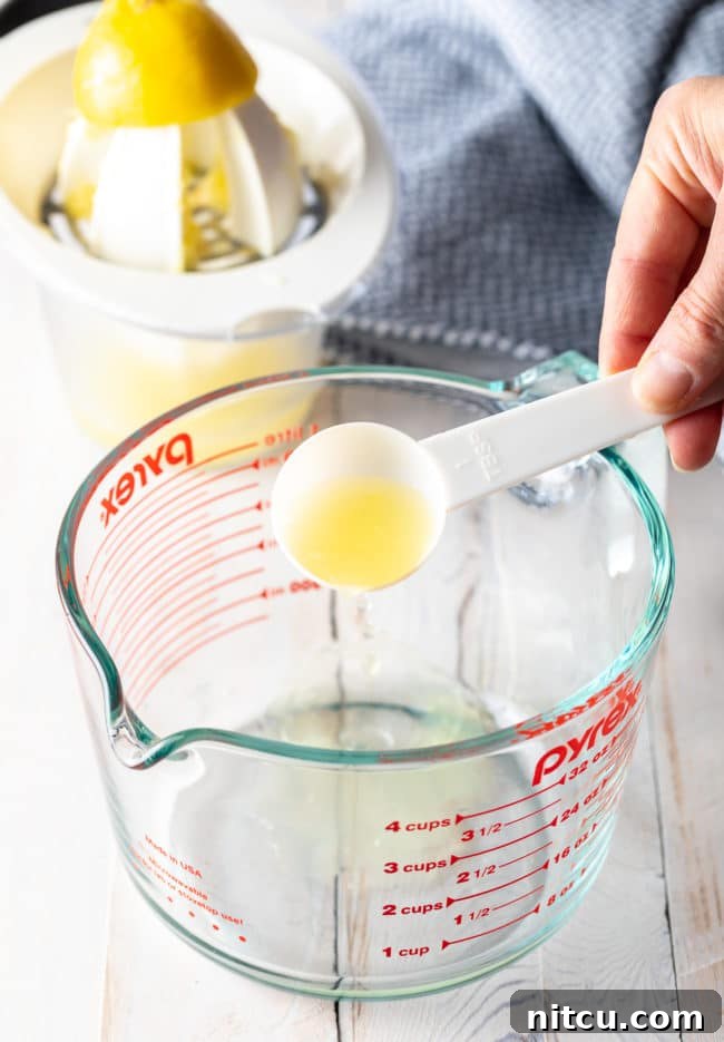 A glass measuring cup as a hand pours lemon juice into the milk.