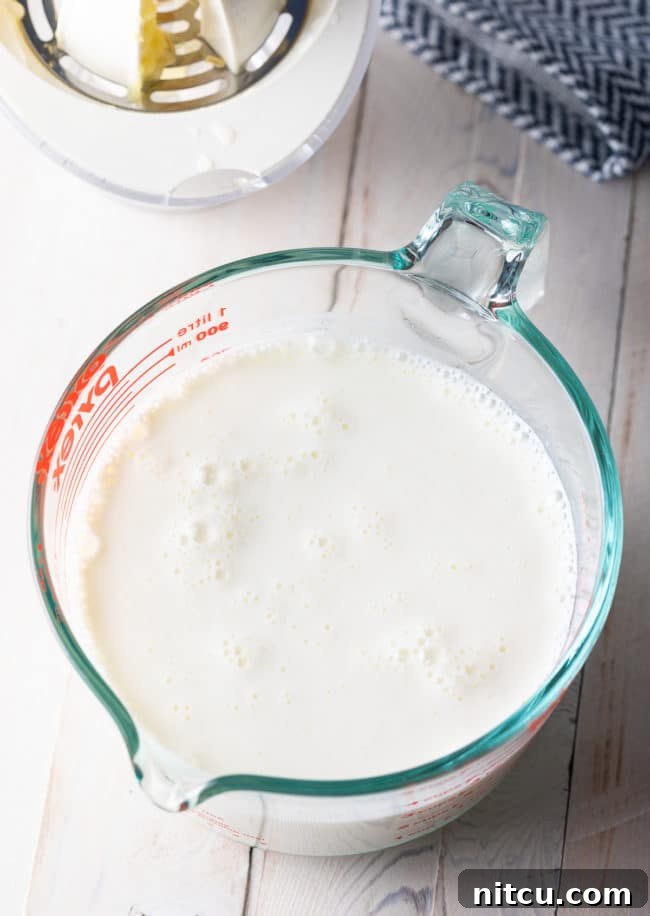Homemade buttermilk substitute actively curdling in a clear glass measuring cup, showing the thickening process.