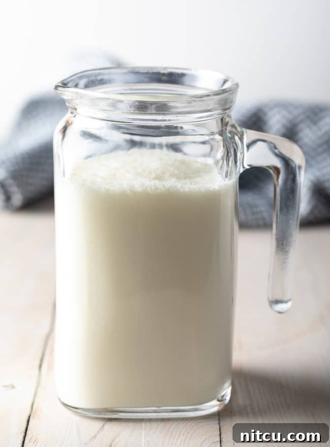 A beautiful side view of a small glass pitcher, perfectly filled with fresh homemade buttermilk.