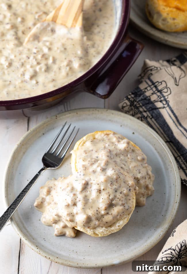 Biscuit on a plate smothered in spicy sausage gravy with a fork. 