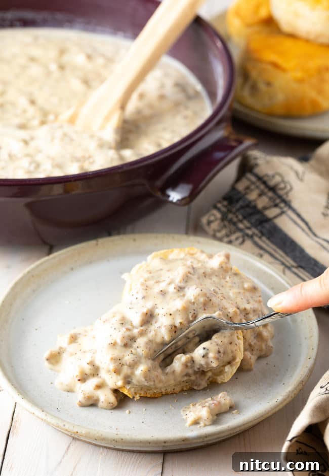 Hand cutting into a biscuit smothered with spicy sausage gravy on a plate. 