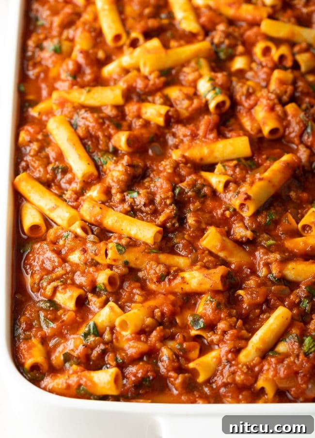 ziti, sauce, sausage, and cheese in baking dish, ready for the oven