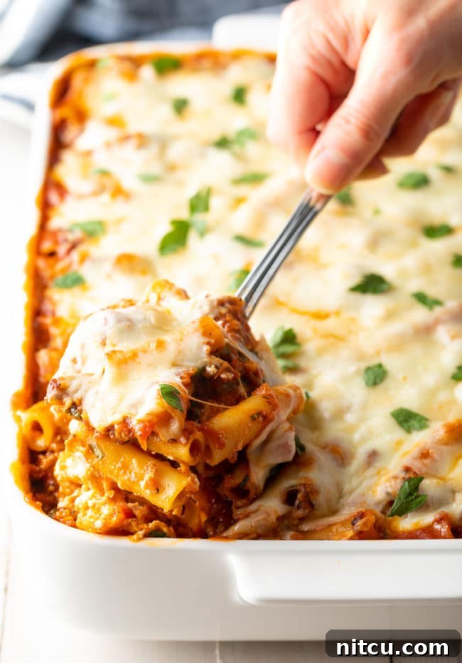 pasta scooped out of baking dish, showing steam and gooey cheese