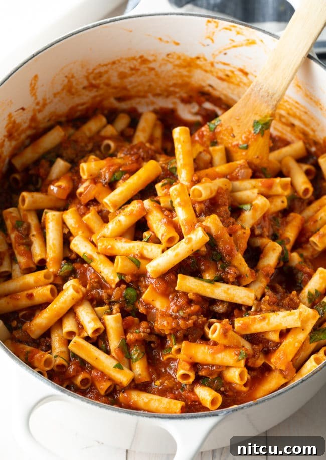 Mixing ziti into meat sauce in a large pot before layering