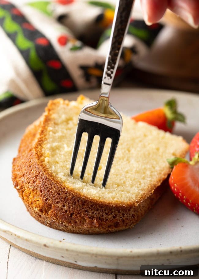 A close-up of a single piece of pound cake on a white dish, with a fork poised for a bite, highlighting its soft texture.