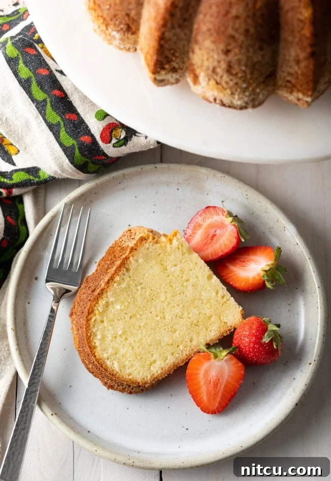 A delectable slice of cream cheese pound cake, perfectly moist and fluffy, resting on a white plate with fresh, ripe strawberries alongside.