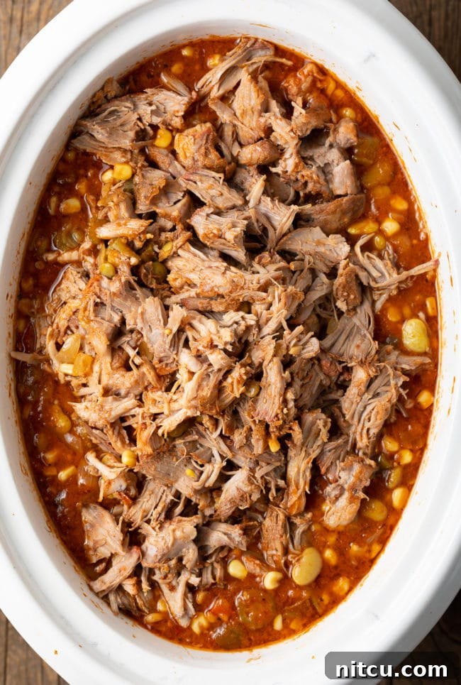 Overhead shot of stew simmering in a crockpot with shredded meat added, showing the rich, thick consistency.