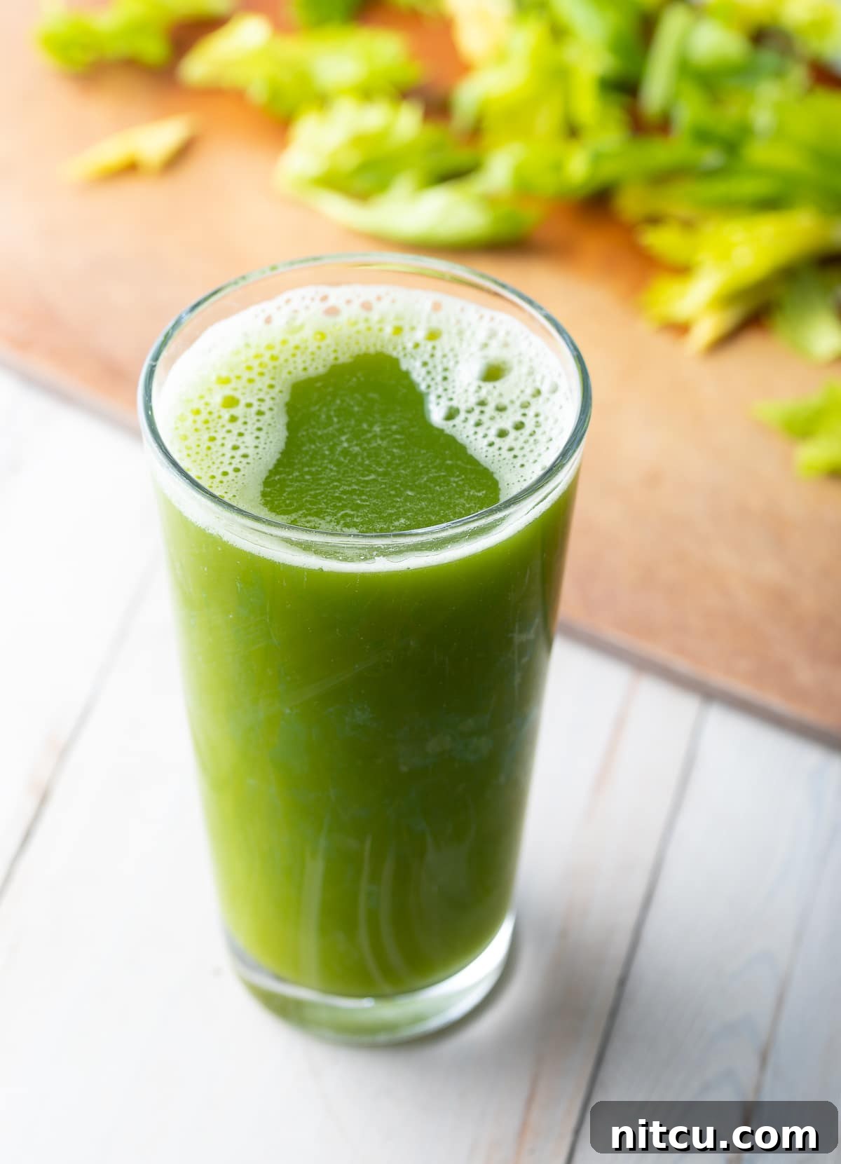 Large glass of celery juice with celery on a cutting board in the background. 