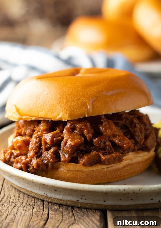 Side view of a mouth-watering BBQ brisket sandwich on a plate, showcasing its tender meat and savory sauce.