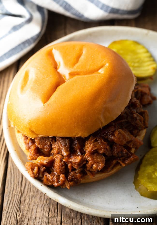 A delicious crock pot brisket sandwich served on a plate with dill pickles, ready to eat.