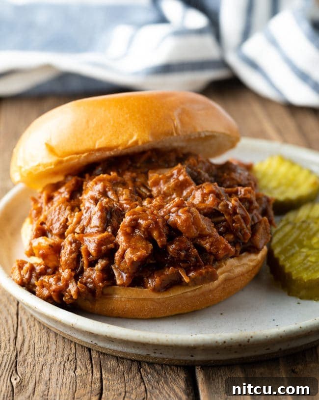 Close-up of a perfectly constructed Chopped Beef Brisket Sandwich, served on a plate with two crisp pickle spears beside it.