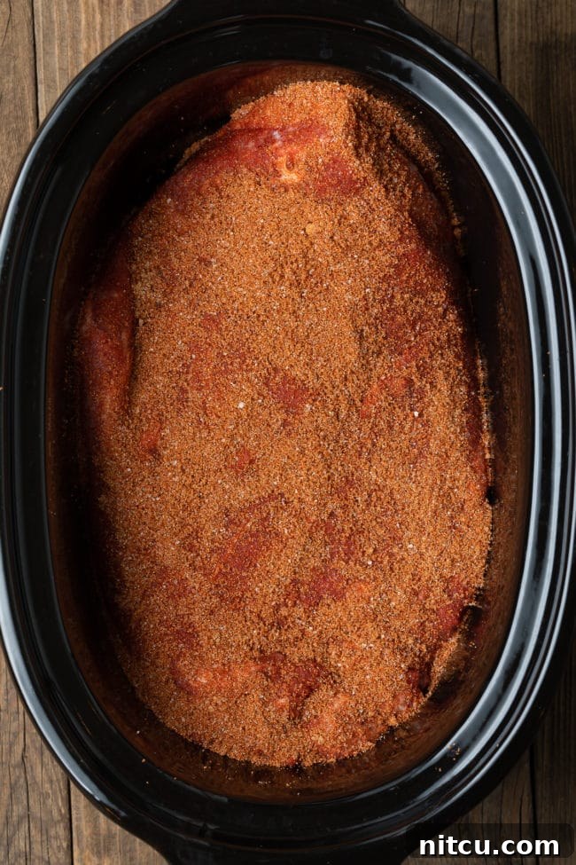 Raw beef brisket seasoned with dry rub, placed inside a slow cooker, ready for cooking.